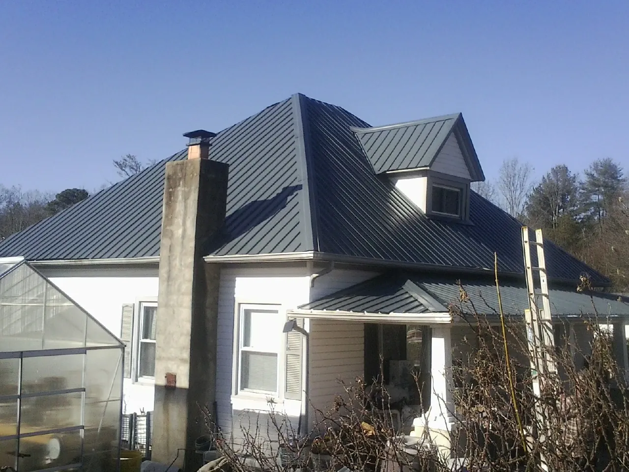 Dark blue standing seam metal roof on a white farmhouse with dormer — Slate & Tile Roof Repair by Roofing Brothers in Estill Springs