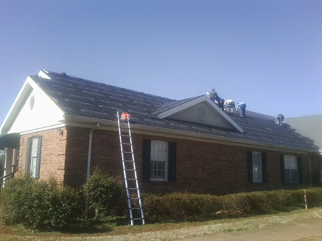 Crew tearing shingles off a brick ranch roof with a ladder set — Metal Roof Repair work by our crew in Estill Springs