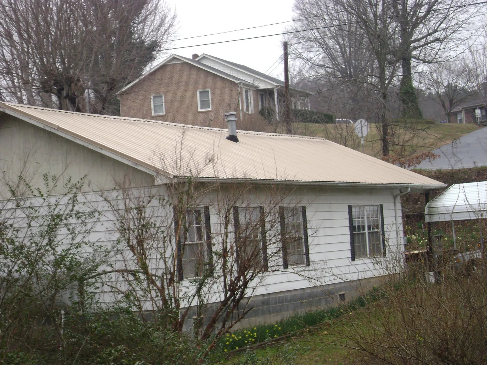 Tan metal roof on a white sided house set into a hillside — Commercial Roofing by Roofing Brothers in Estill Springs